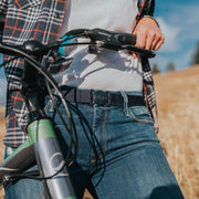 Woman wearing a Denim Navy Jelt elastic belt with jeans and flannel, while walking bike